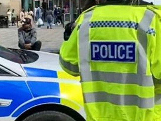 A police officer is photographed from the rear wearing a high viz jacket with POLICE on the back